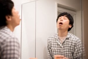 japanese man in pajamas wearing toothbrush gargle in bathroom at homehe carefully gargles stockpack istock scaled 1